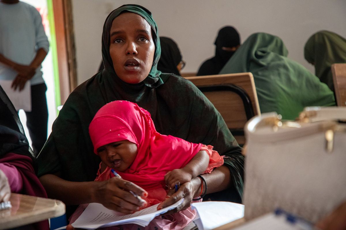 A mother taking notes in class with her daughter on her lap
